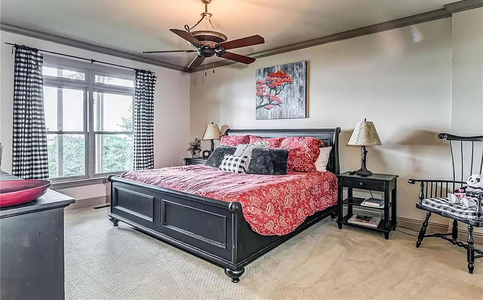 Un dormitorio con cama, dos mesitas de noche, una silla, ventilador de techo y ventana con cortinas.