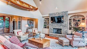 A spacious living room with a stone fireplace, comfortable seating, and a large TV mounted on the wall. - Eagles View - Gorgeous Mountain Views + Luxury Interiors + Telescope + Library (Dawsonville)