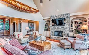 A spacious living room with a stone fireplace, comfortable seating, and a large TV mounted on the wall.