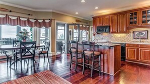 A spacious kitchen with wooden cabinets, a central island, and a dining area with chairs. - Eagles View - Gorgeous Mountain Views + Luxury Interiors + Telescope + Library (Dawsonville)