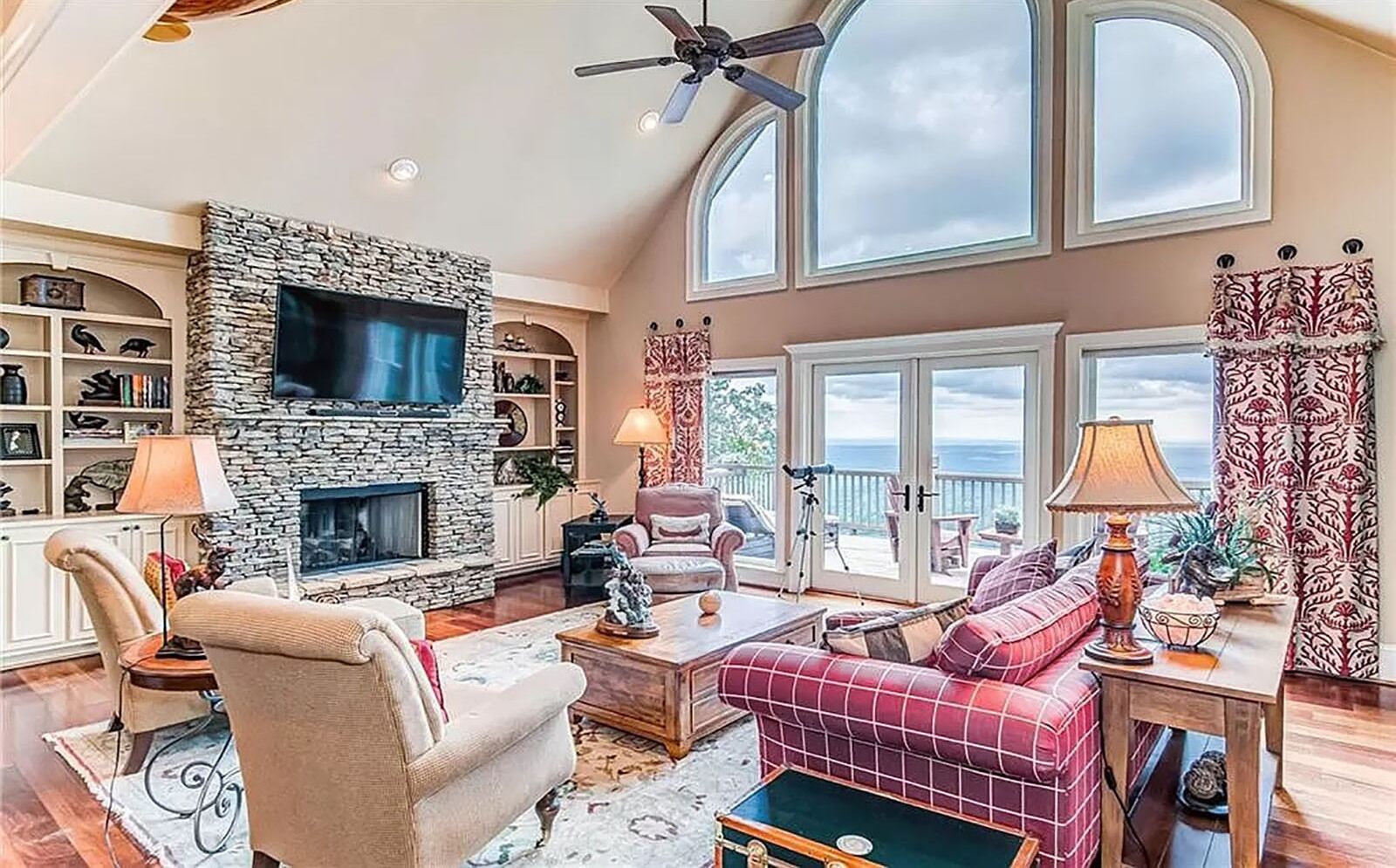 A spacious living room with a stone fireplace, a large TV, and a cozy seating area with a red sofa and armchairs.