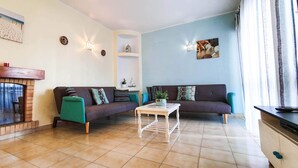 A living room with a fireplace, two sofas, a coffee table, and decorative wall art. - Apartment - Sleeps 2, Parking & Pool Access (Albufeira)