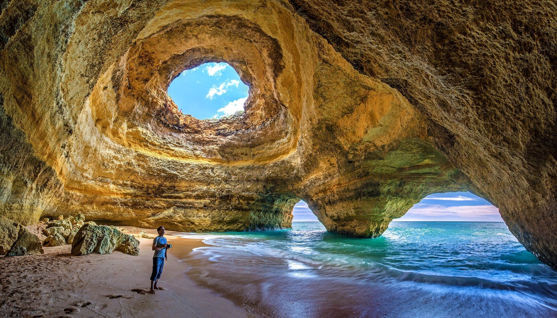 A natural rock formation with a circular opening, a sandy beach, and the ocean.