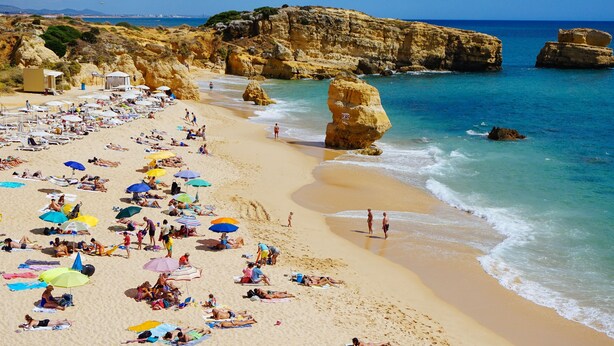 A beach with numerous umbrellas and people sunbathing. - Apartment - Sleeps 2, Parking & Pool Access (Albufeira)