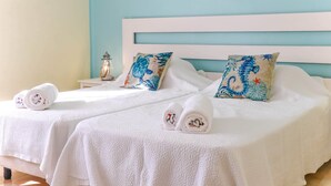 A hotel room with two beds, each with a white headboard and a blue and white patterned pillow. There are towels neatly rolled on the beds. - Apartment - Sleeps 2, Parking & Pool Access (Albufeira)