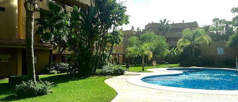 A pool area with a curved pathway, palm trees, and a building with balconies.