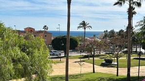 A coastal view with a parking area, palm trees, and a building in the background. - La Cala 2 Bedroom Apt with Sea View and Pool View (La Cala de Mijas)