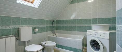 A compact bathroom with a skylight, a bathtub, a toilet, a bidet, and a washing machine.