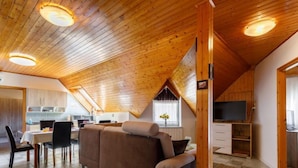 Acogedor espacio tipo loft con techo de madera, un sofá, una mesa de comedor y una cocina al fondo.