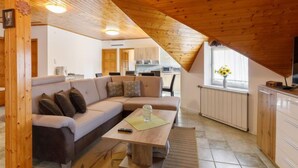 Un espacio habitable estilo loft acogedor, con techo de madera, un sofá, una mesa de centro y una cocina visible al fondo.