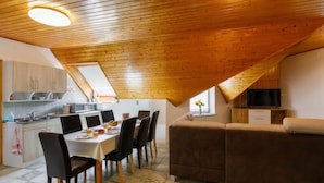 Un dormitorio acogedor en el ático con techo de madera, un área de comedor con mesa y sillas, un sofá y una televisión.