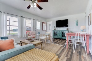 Relax in this spacious living area with a high ceiling, featuring a large window, TV, and comfortable seating.