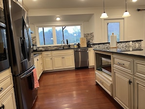 A modern kitchen with white cabinetry, stainless steel appliances, and a large window providing natural light.