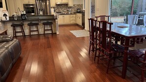 Una cocina amplia con piso de madera, un comedor con una mesa grande y sillas, y vistas al exterior.