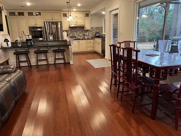 A spacious kitchen with wooden flooring, a dining area with a large table and chairs, and a view of the outdoors.