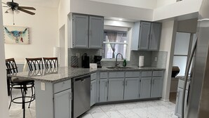 Eine moderne Küche mit grauen Schränken, einer Granit Arbeitsplatte, einem Geschirrspüler und einem Kühlschrank.