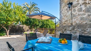 Un área de comedor al aire libre con una mesa para dos, un mantel azul y un frutero.