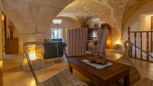 Un interior con arcos de piedra, una mesa de madera, sillas a rayas y una alfombra tejida.