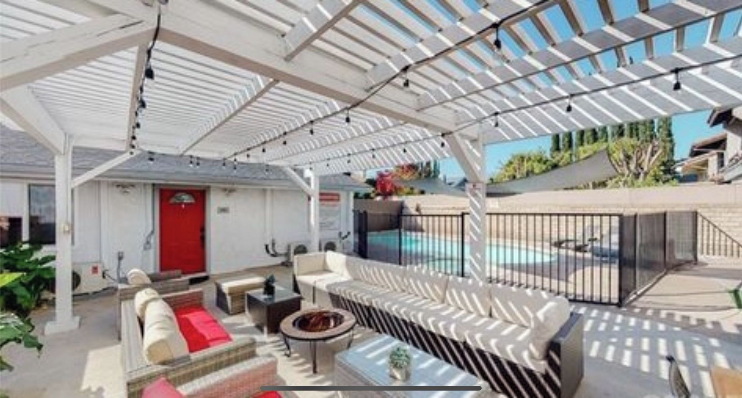 Un espacio al aire libre techado con asientos, una piscina y una puerta roja.