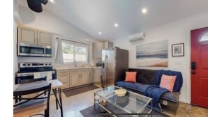 Un espace de vie compact comprenant un coin cuisine, un coin repas et un espace détente avec un canapé et une porte rouge.