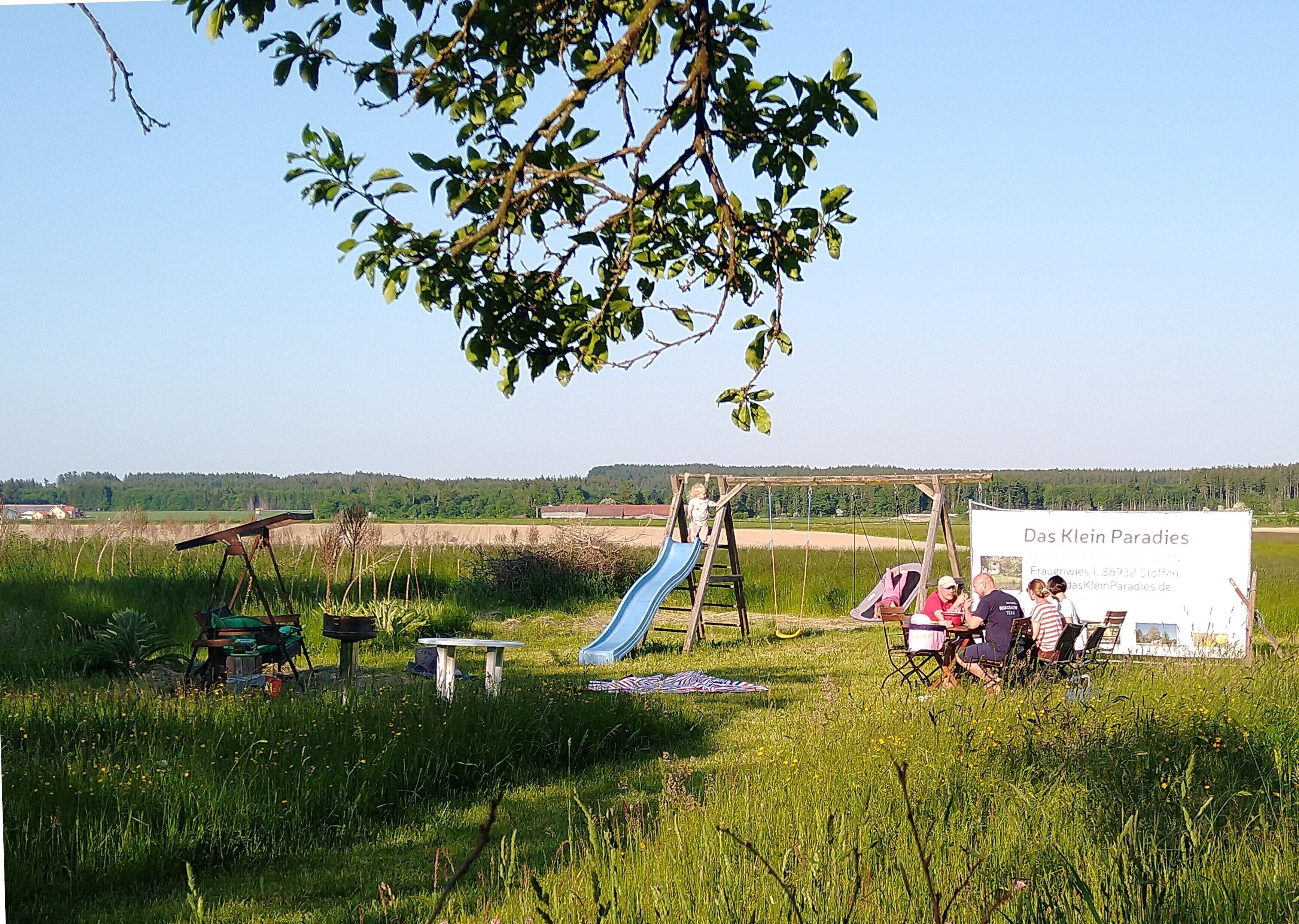 A grassy outdoor area with a swing set, a slide, and a picnic table.