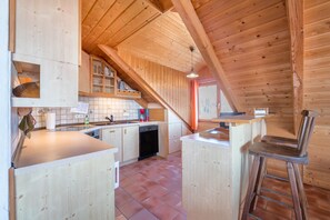 Cocina con armarios de madera, lavavajillas y barra con taburete.