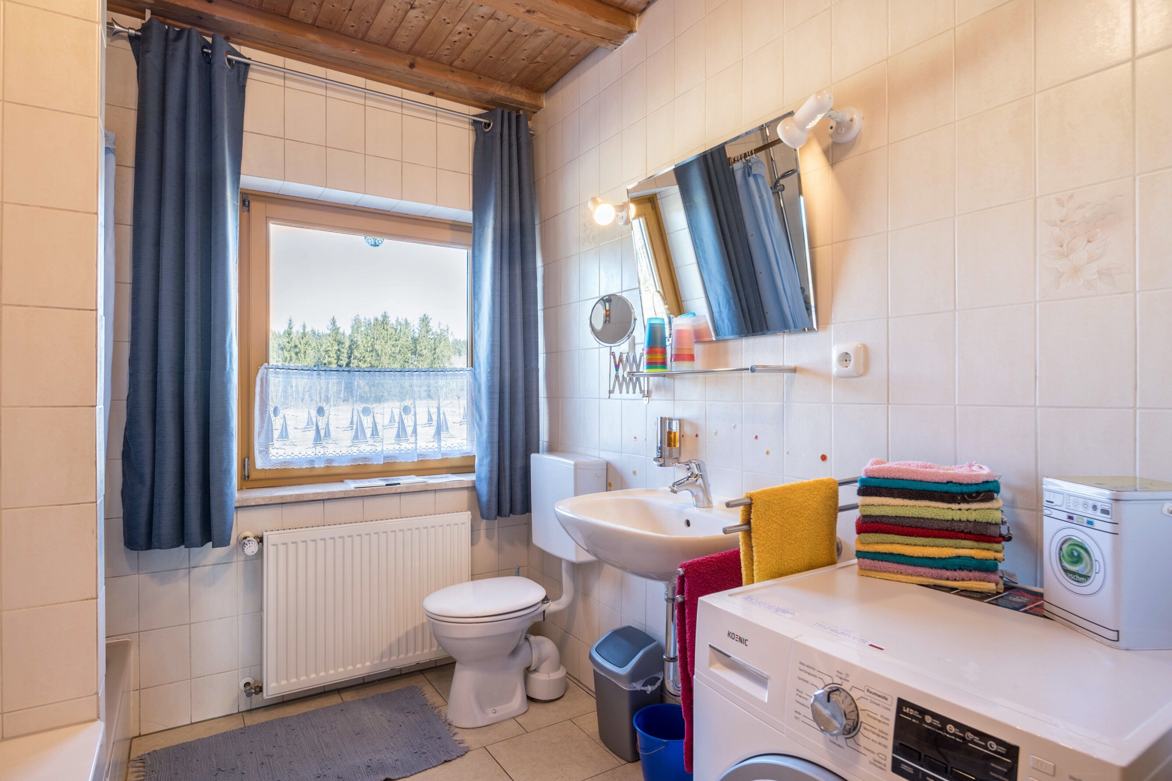 Une salle de bain comprenant des toilettes, un lavabo, un miroir, une fenêtre et un lave-linge.