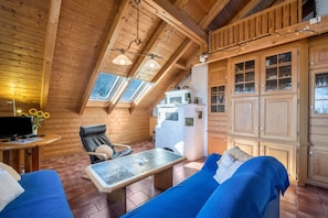 Interior acogedor de una cabaña de madera con comedor, sofá, televisor y zona de cocina.