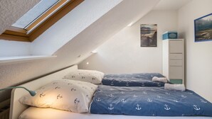 Un dormitorio con tragaluz, una cama con ropa de cama estampada con anclas, una mesita de noche y un mueble de pared.