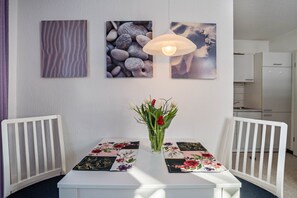 Et spiseområde med et hvidt bord, to hvide stole, en vase med blomster og to billeder hængt på væggen.