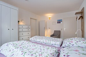 Et soveværelse med to senge, et kommode, en stol og et skab.