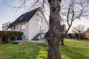 Un immeuble résidentiel à la façade en briques, avec un escalier menant à l’entrée et une pelouse verdoyante.