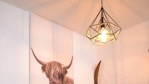 Una mesa de comedor de madera con dos sillas, una botella de vino y dos copas. Un cuadro de un toro está en la pared sobre la mesa.