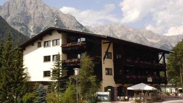 Un hotel de estilo alpino tradicional, con balcones y un paisaje montañoso de fondo.