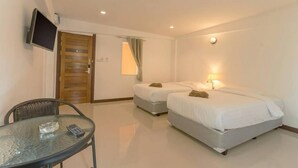 A hotel room with two single beds, a glass table with a remote control, a TV mounted on the wall, and a wooden door. - Guyana Saikaew (Rayong)