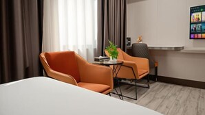 A hotel room with a bed, two orange chairs, a small table with a plant, a TV on a stand, and a wall-mounted artwork. - Park Lane Hotel (Jiangmen Shuinan) (Jiangmen)