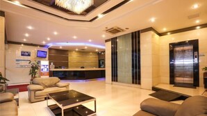 A modern lobby with a reception desk, seating area, and an elevator. - Park Lane Hotel (Jiangmen Shuinan) (Jiangmen)