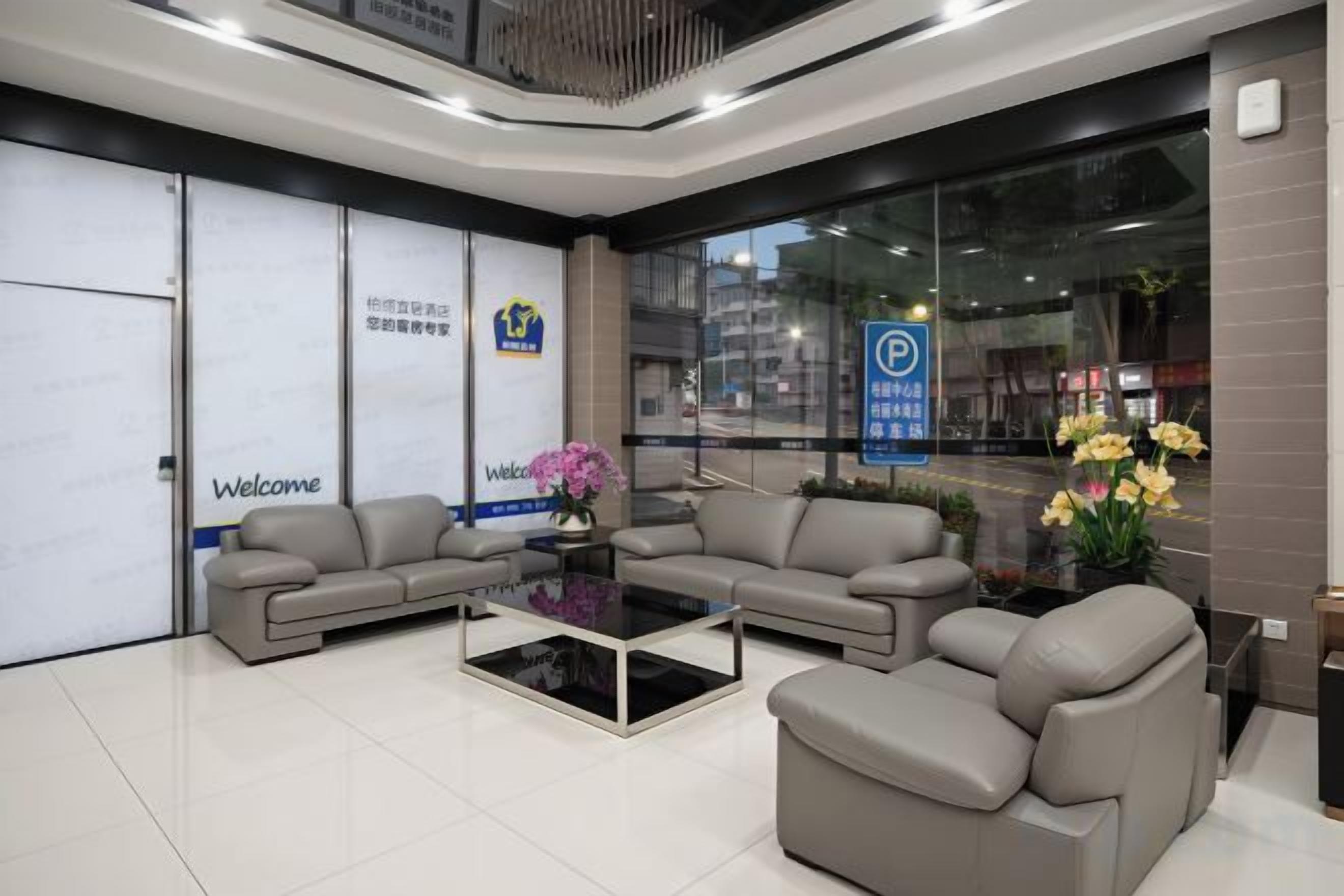 A reception area with a sofa, a coffee table, and a vase of flowers. There are signs on the wall and a window with a view of the street.