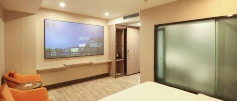 Una habitación de hotel moderna con una cama grande, un televisor de pantalla plana en la pared, un sillón naranja y un armario de madera.