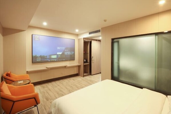 A modern hotel room with a large bed, a flat-screen TV mounted on the wall, an orange chair, and a wooden wardrobe. - Park Lane Hotel (Jiangmen Shuinan) (Jiangmen)