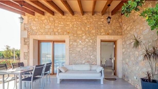 A stone-walled room with a sofa, a dining table with chairs, and a potted plant. - El Rafal de Son Alberti Petitona (Buger)