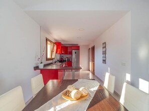 A modern kitchen with red cabinets, a stainless steel refrigerator, and a dining area with a wooden table and white chairs. - El Rafal de Son Alberti Petitona (Buger)