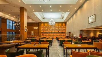 A spacious library with multiple tables and chairs, a central bookshelf, and a bar area.