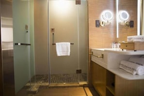 Une salle de bain d’hôtel avec une douche à parois de verre, un meuble-lavabo avec un miroir et un porte-serviettes sur lequel est posée une serviette blanche.