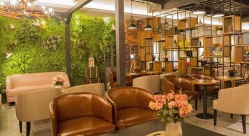 Un rincón de descanso acogedor con sofás de cuero, una pared verde con plantas y una estantería de madera.