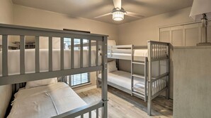 Ein Schlafraum mit Etagenbetten, Deckenventilator, Fenster mit Jalousien und einer Lampe auf einem Nachttisch.