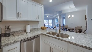 A modern kitchen with white cabinetry, granite countertops, stainless steel appliances, and a dining area with a chandelier. - Water Views + Pool Access: Lake Ozark Escape! (Lake Ozark)