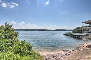 Blick auf einen See mit einem Steg, der ins Wasser hineinreicht, umgeben von viel Grün und einem klaren Himmel.