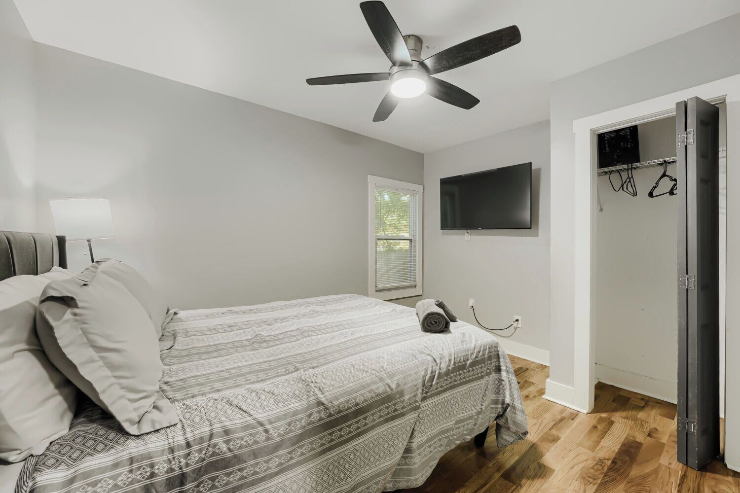 Une chambre à coucher avec un lit, un ventilateur de plafond, une télévision et une porte donnant sur une autre pièce.