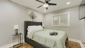 Ein Schlafzimmer mit einem Bett, einem Deckenventilator, einem Fenster mit Jalousien und einem Wandbild.